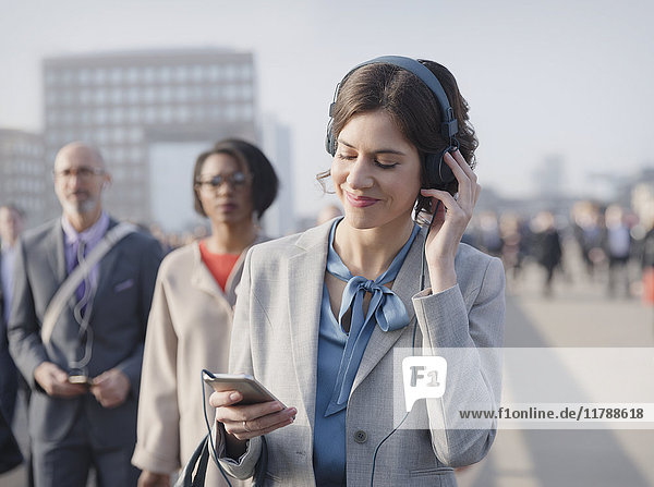 Geschäftsfrau lächelt  Musik hören mit Kopfhörer und Smartphone auf der städtischen Fußgängerbrücke