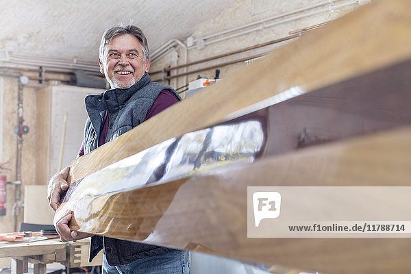 Lächelnder Schreiner mit fertigem Holz in der Werkstatt
