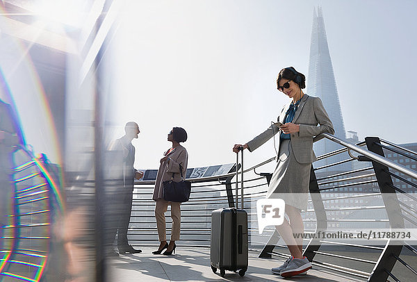 Geschäftsfrau mit Koffer  Musik hören mit Smartphone und Kopfhörer  London  UK
