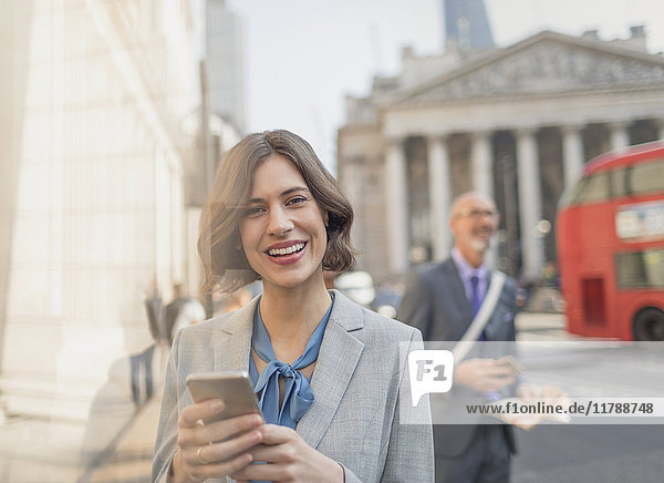 Portrait lächelnde Geschäftsfrau  SMS mit Handy in der City Street  London  UK
