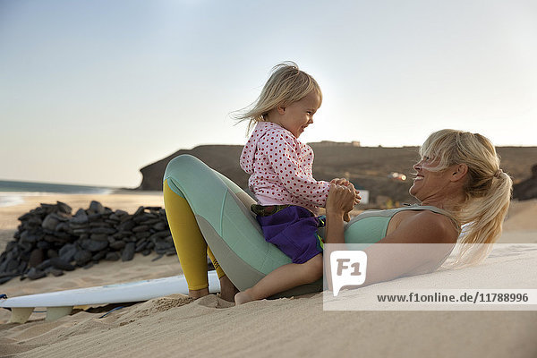 Spanien  Fuerteventura  glückliche Mutter und Tochter am Strand neben dem Surfbrett bei Sonnenuntergang