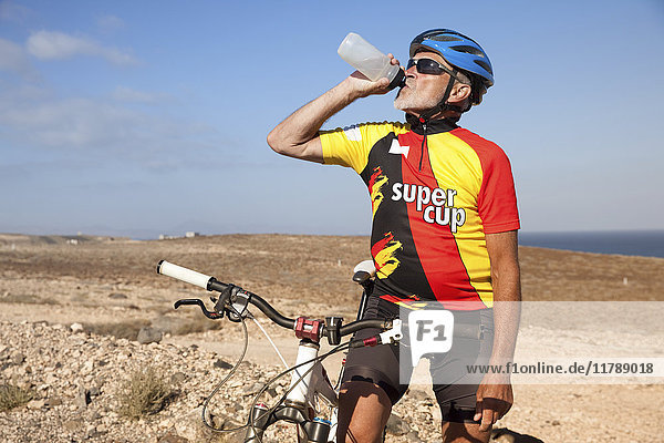 Spain  Canary Islands  Fuerteventura  senior man with mountainbike drinking from bottle