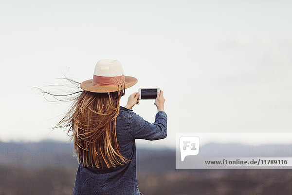 Rückansicht der rothaarigen Frau beim Fotografieren mit dem Smartphone in der Natur