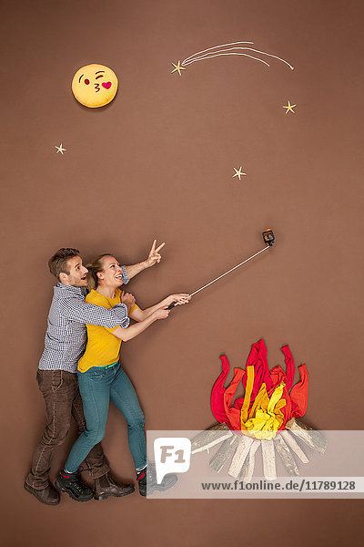 Couple roasting sausages at the campfire and taking a selfie