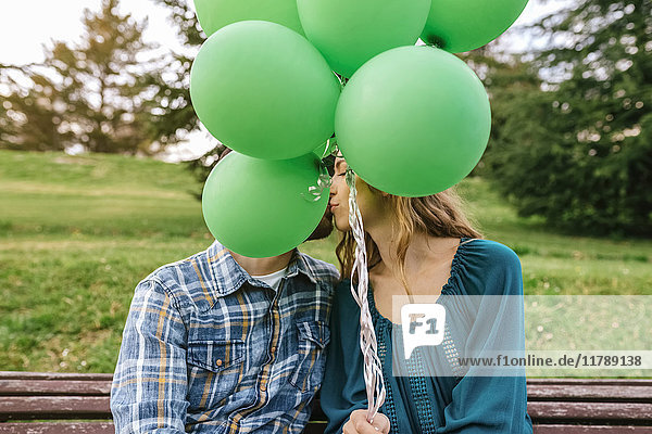 Junges Paar küsst sich hinter grünen Luftballons