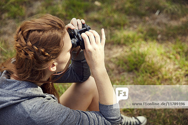 Young woman sitting on a meadow using binoculars