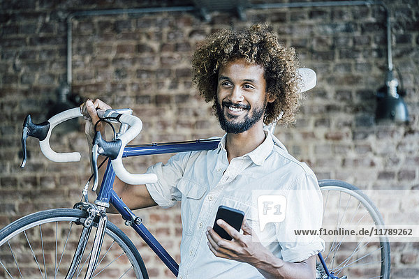 Lächelnder junger Mann mit Fahrrad und Handy