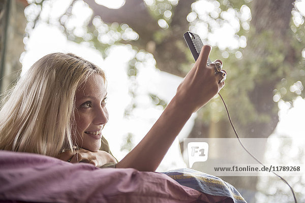 Lächelnde junge Frau  die auf dem Bett liegt und Selfie mit dem Handy nimmt