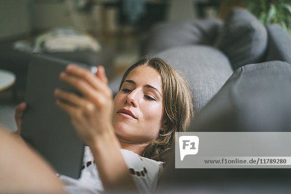 Entspannte junge Frau auf der Couch liegend mit Tablette