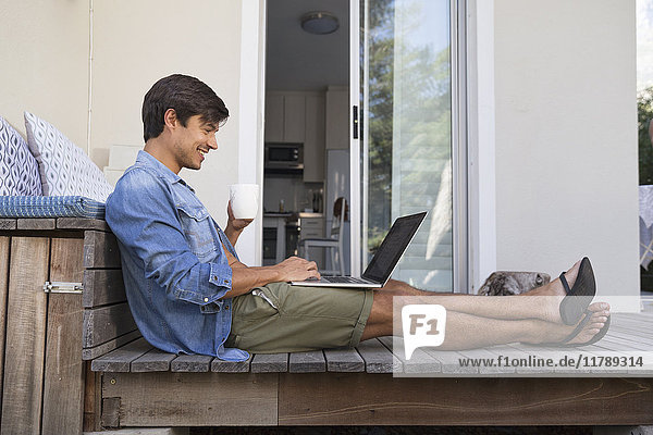 Mann sitzt auf der Terrasse mit Laptop