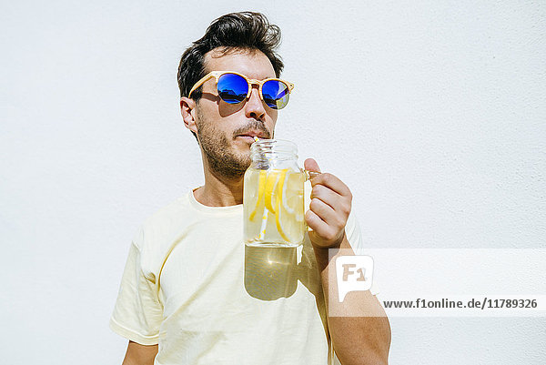 Man with sunglasses drinking lemonade in front white wall