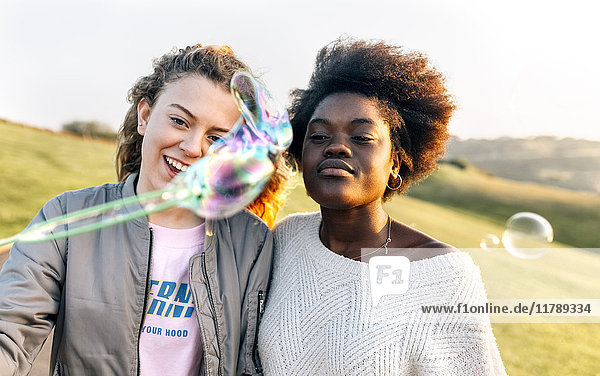 Two best friends making soap bubbles outdoors at sunset