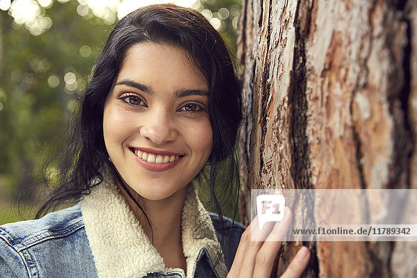 Porträt der lächelnden jungen Frau neben dem Baumstamm