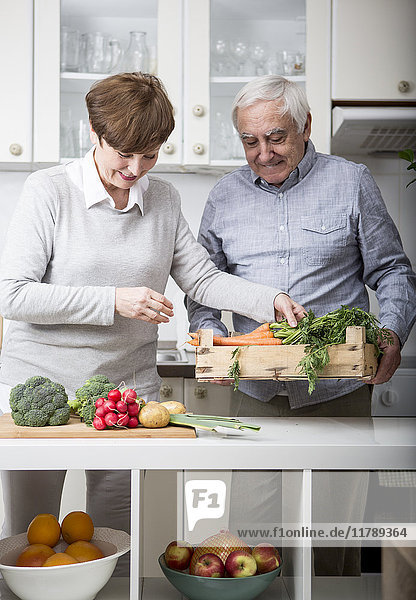 Seniorenpaar steht in der Küche und packt frisches Gemüse aus.