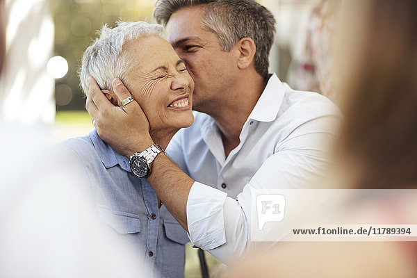 Erwachsener Sohn küsst glückliche Seniorin im Freien