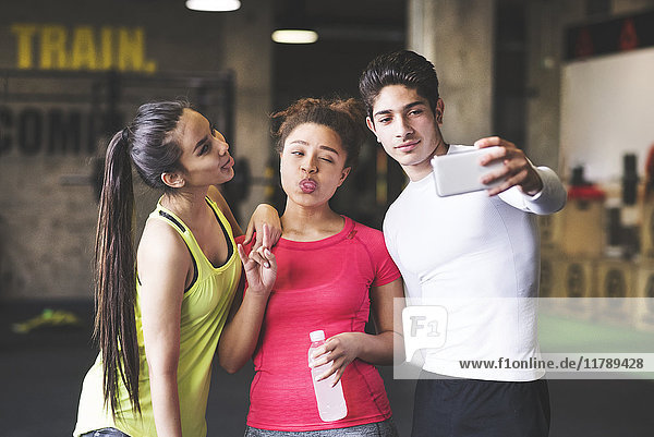 Drei verspielte junge Leute,  die einen Selfie im Fitnessstudio nehmen.