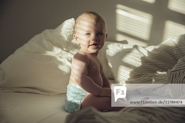 Baby Junge sitzt im Bett im Schatten und Sonnenlicht