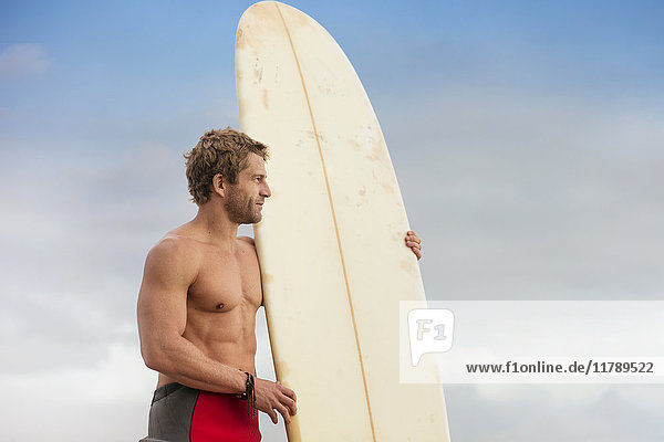 Mann steht am Strand mit Surfbrett und genießt die Aussicht