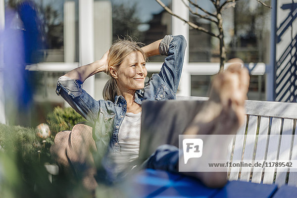 Smiling woman with laptop relaxing on garden bench