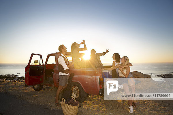 Happy young people outside pick up truck at the coast at sunset