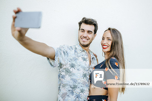 Couple taking a selfie with smartphone in front of white wall