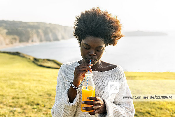 Junge Frau trinkt Orangensaft an der Küste