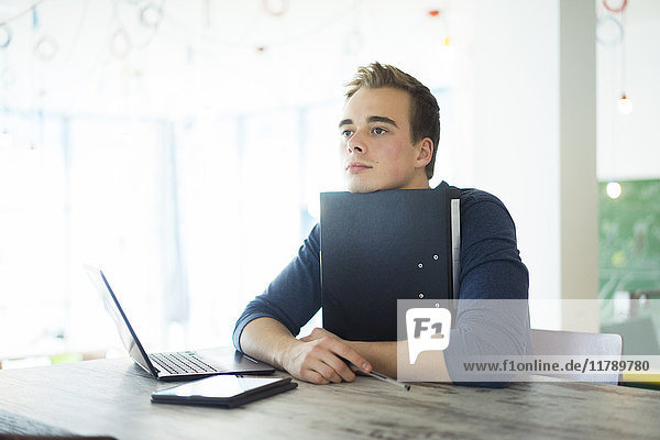 Portrait eines gelangweilten Schülers mit Datei  Laptop und Tablett