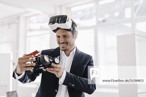 Lächelnder Geschäftsmann mit VR-Brille beim Blick auf Spielzeug-Rennwagen