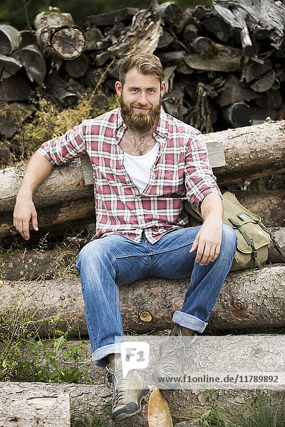 Porträt eines bärtigen Mannes  der auf einem Holzstapel sitzt.