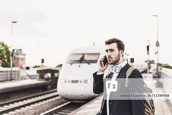 Young man using cell phone on platform as train coming in