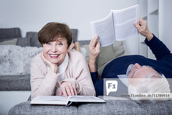 Seniorenpaar auf der Couch liegend  Bücher lesend