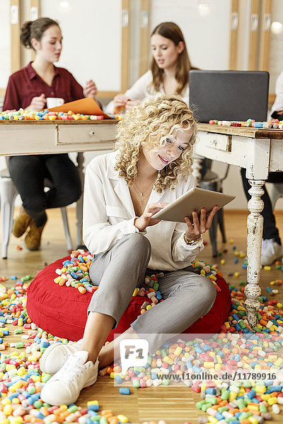 Frau mit Tablette im Büro umgeben von bunten Polystyrolteilen