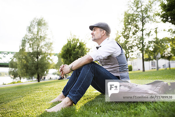 Mature businessman in the city park sitting on grass
