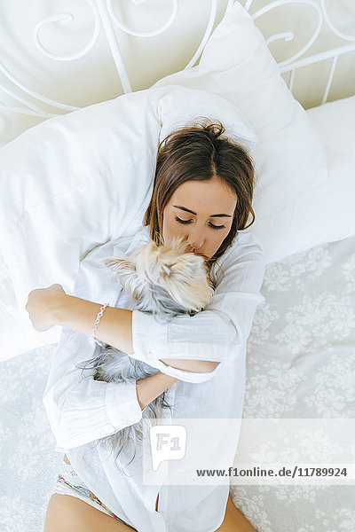Frau auf dem Bett liegend mit Umarmen und Küssen ihres Yorkshire Terriers,  Draufsicht
