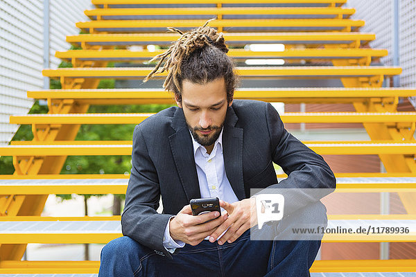 Junger Geschäftsmann mit Dreadlocks auf der Treppe mit Smartphone