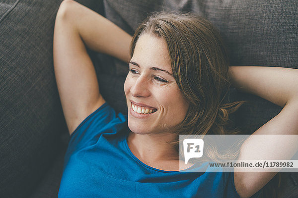 Smiling young woman lying on couch at home