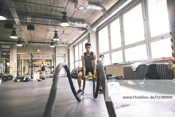 Young athlete exercising with ropes in gym