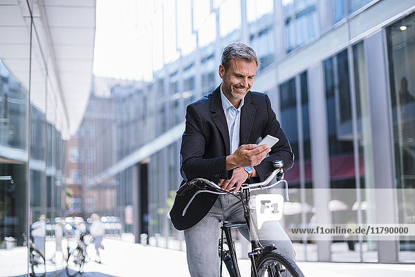 Lächelnder Geschäftsmann mit Fahrrad und Handy in der Stadt