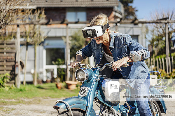 Glückliche Frau auf Oldtimer-Motorrad mit VR-Brille