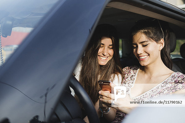 Zwei glückliche junge Frauen  die das Handy im Auto anschauen.