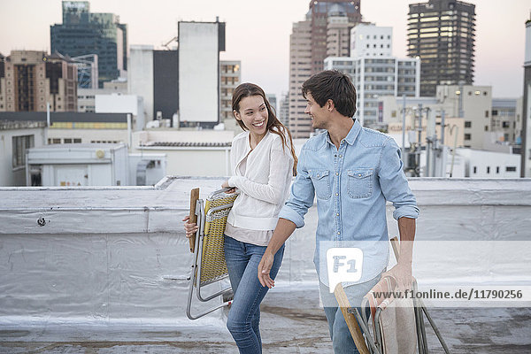 Young couple carrying folding chairs on a rooftop terrace