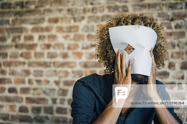 Man with beard and curly hair hiding behind paper mask