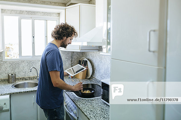 Man cooking in kitchen while looking at tablet