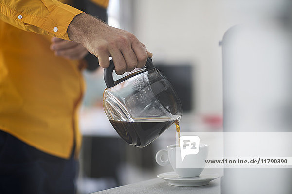 Mitarbeiter mit Schleuder  der bei der Arbeit Kaffee in die Tasse schüttet.
