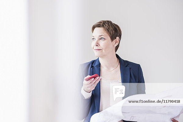 Confident real estate agent holding plan and cell phone