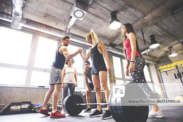 Group of young fit people motivating woman weightlifting in gym