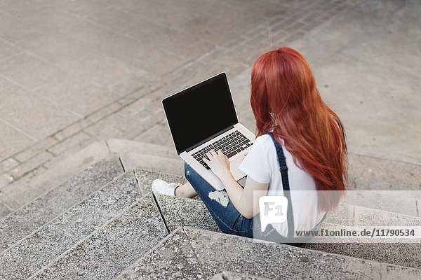 Rothaarige Frau auf der Treppe sitzend mit Laptop