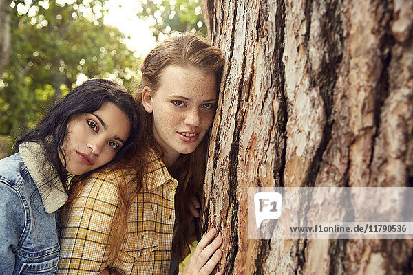 Portrait of two young women leaning against tree trunk