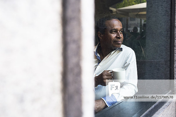 Nachdenklicher Mann in einem Café mit Tasse Kaffee durchs Fenster schauend