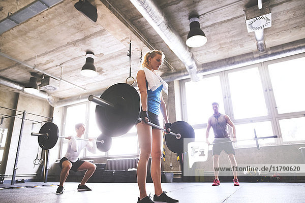 Young woman with training partners lifting barbell in gym
